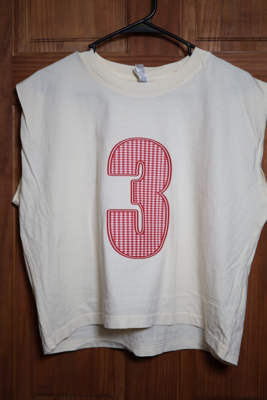 Ivory muscle tank featuring a large red and white gingham varsity number 3 outlined in red.