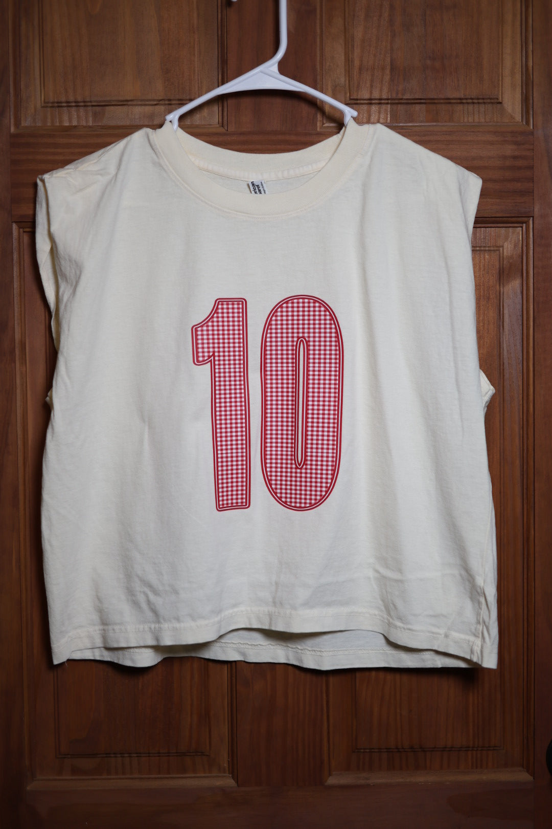 Ivory muscle tank featuring a custom red and white gingham varsity number 10 with varsity-inspired styling.