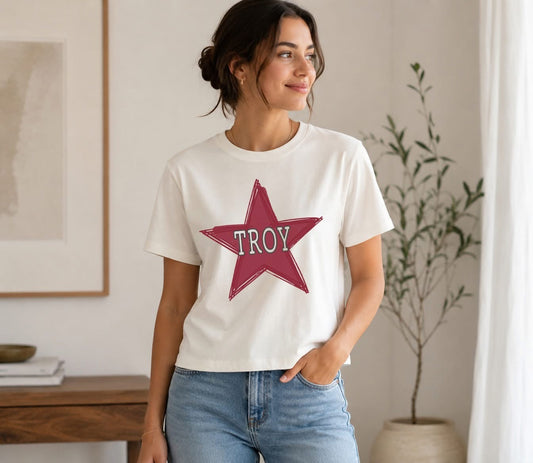 Lifestyle photo of a woman wearing a white short-sleeve t-shirt featuring a large cardinal red sketch-style star graphic with TROY text centered on the front.