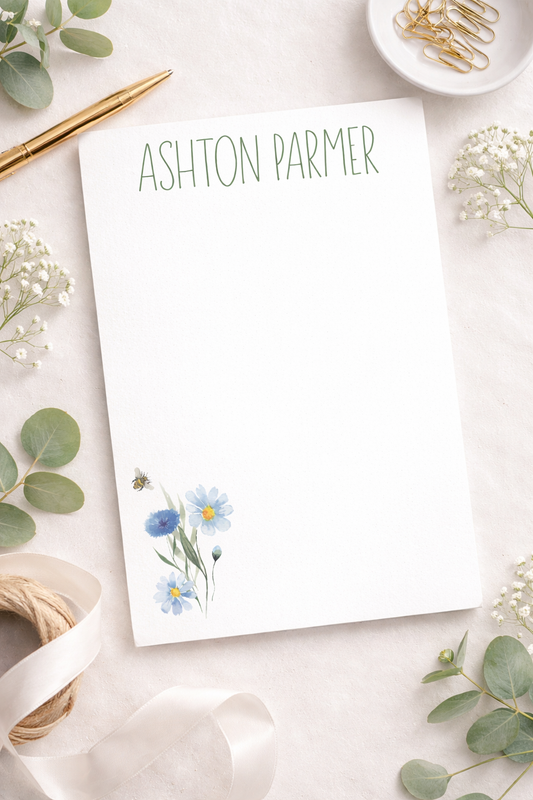 Notepad with floral design and 'Ashton Parmer' (customizable) text on a decorative surface with flowers and ribbons.