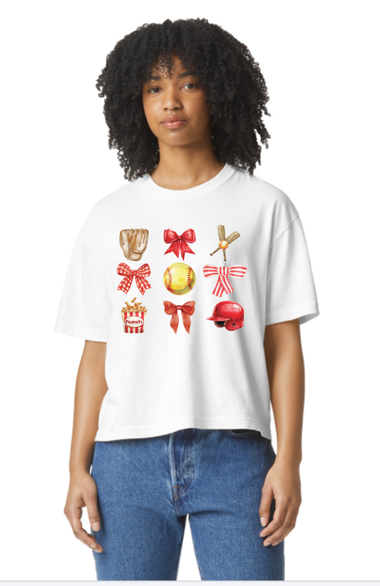 White t-shirt with colorful softball graphics (bows, softball, glove, bat, helmet, popcor) on a white background